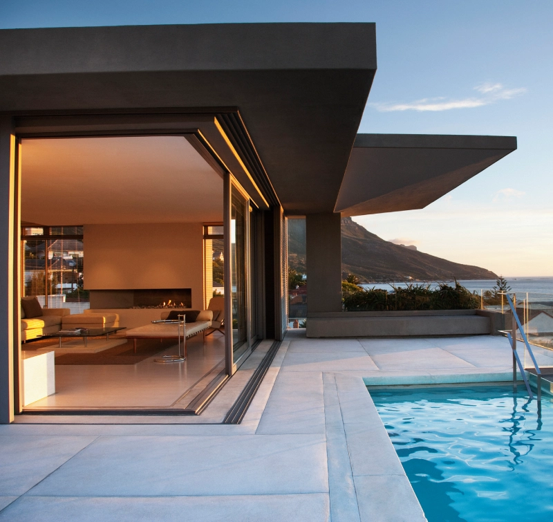 Modern house with sliding glass doors opening to a pool at sunset.