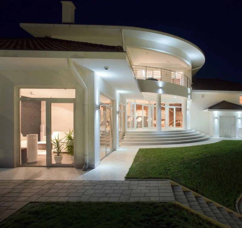 Modern house exterior at night with illuminated entrance and curved roof design.